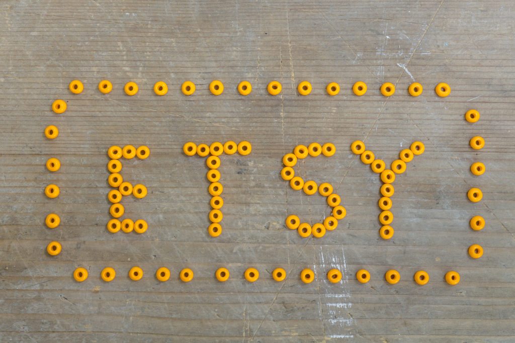 Etsy logo written in orange beads on a wooden background